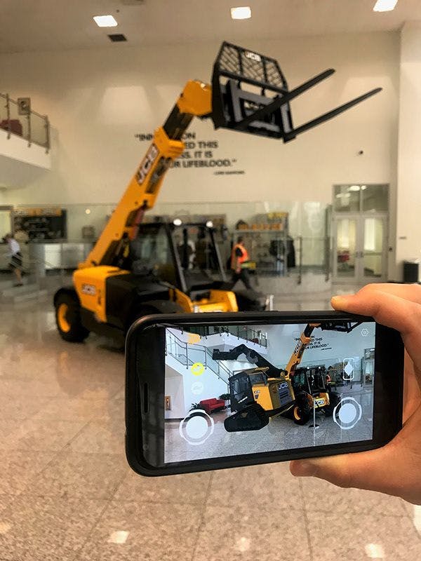 Someone using their phone to compare the augmented reality Teleskid with a real Telehandler.