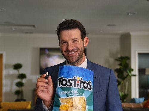 Tony Romo smiling with his ear piece in his hands eating Tostitos chips.